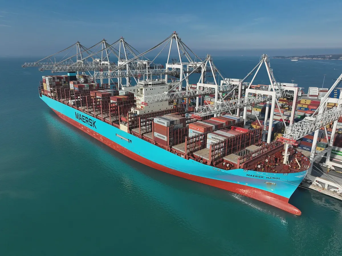 A container ship under ship-to-shore gantry cranes at berth: a Class 9 booking needs the carrier's dangerous goods desk approval five to ten working days before the vessel